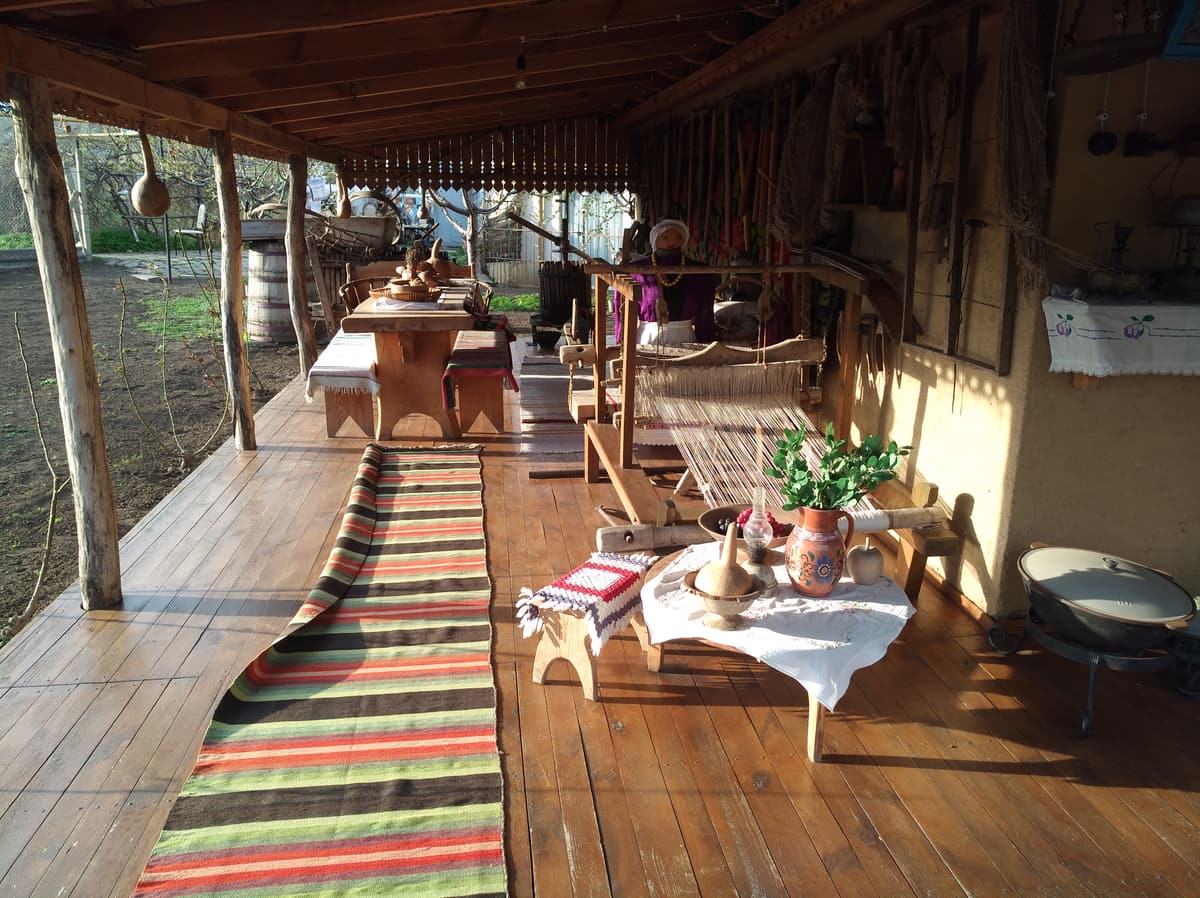 Eine Holzveranda mit gestreiften Teppichen und niedrigen Tischen im Gagauz Sofrası